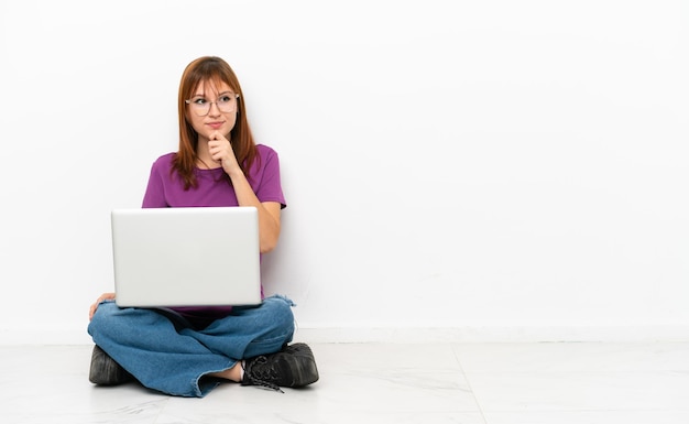 Roodharig meisje met een laptop die op de grond zit en omhoog kijkt