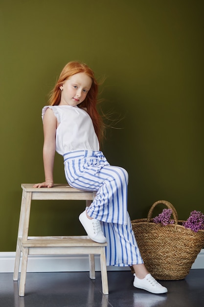 Roodharig meisje met een mand met bloemen poseren op een olijf achtergrond. lente portret van een roodharig meisje met blauwe ogen. haar in de kleur van vuur, noors tienermeisje