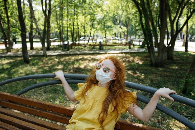 Roodharig meisje met een wegwerpmasker loopt in een stadspark.