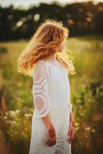 Roodharig meisje met krullen in boho-stijl kleding met mehendi tekeningen op haar handen in een zomer veld.