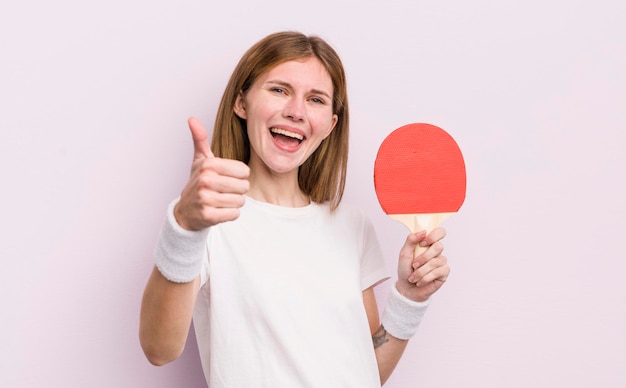 Roodharig mooi meisje dat trots positief glimlacht met duimen omhoog pingpongconcept