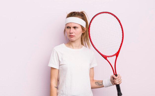 Roodharig mooi meisje voelt zich verdrietig, boos of boos en kijkt naar het tennisconcept aan de zijkant