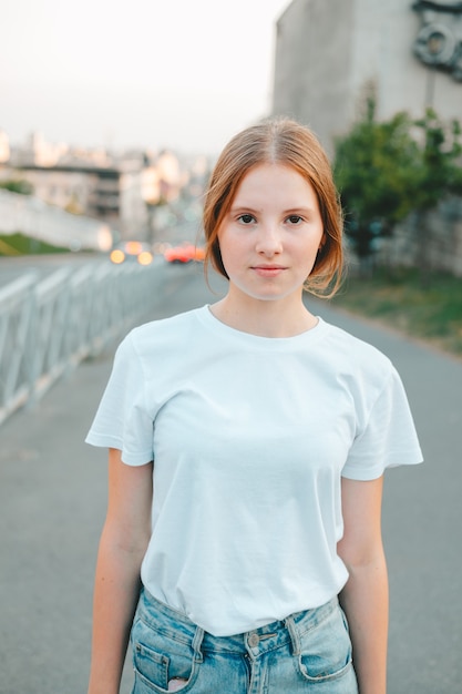 Roodharig tienermeisje in een wit T-shirt en spijkerbroek loopt door de stad
