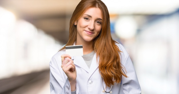 Roodharige artsenvrouw die een creditcard in het ziekenhuis houden