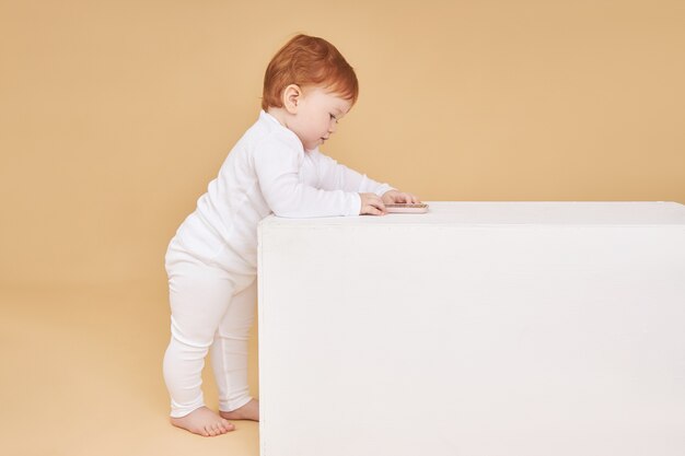 Roodharige babymeisje speelt op beige. Grote moedervlek op het voorhoofd, niet zoals iedereen