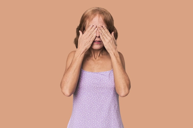 Roodharige blanke vrouw van middelbare leeftijd in de studio die bang is om haar ogen met haar handen te bedekken.