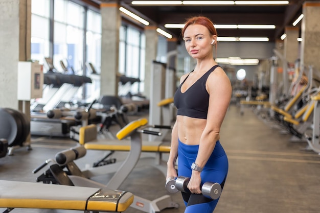 Roodharige fitte vrouw die traint met halters in haar handen in een moderne sportschool