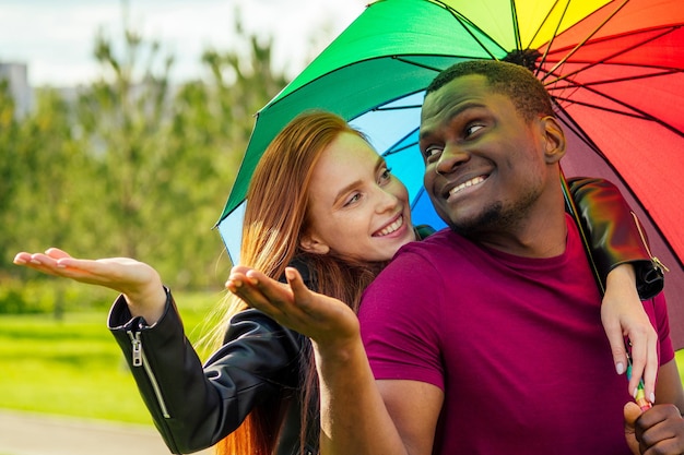 Roodharige gembervrouw en afro-amerikaanse man die dicht bij elkaar staan onder paraplu in zomerpark