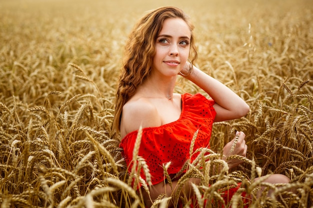 Roodharige jonge vrouw in rode jurk op tarweveld gelukkig meisje met krullend haar in veld zoete glimlach van l...