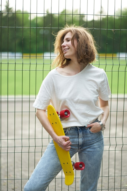 Roodharige jonge vrouw met skateboard in de buurt van hek