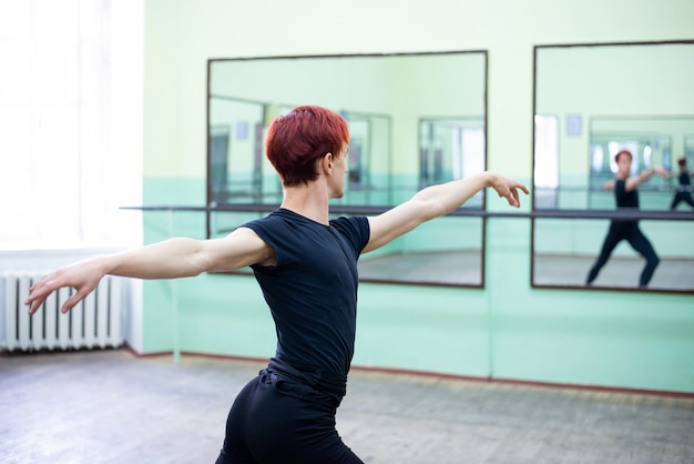 Roodharige jongeman die danst in het midden van balletstudio voor grote spiegels