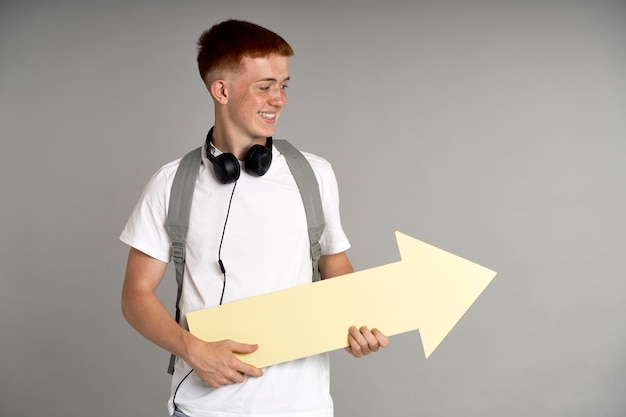 Roodharige jongen met schooltas die een groot pijlteken vasthoudt en ernaar kijkt