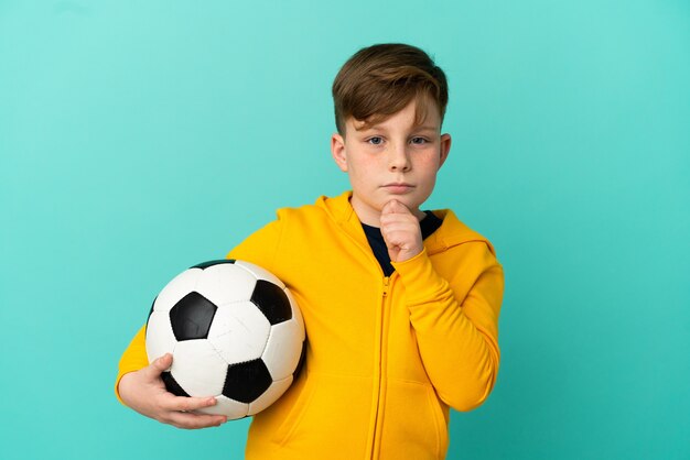 Roodharige jongen voetballen geïsoleerd op blauwe achtergrond en opzoeken