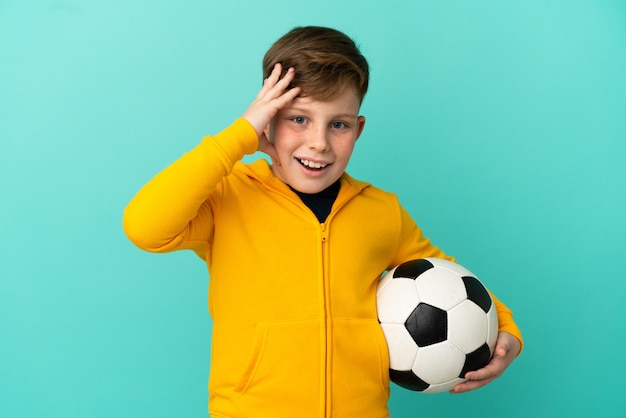 Roodharige jongen voetballen geïsoleerd op blauwe achtergrond met verrassing expression