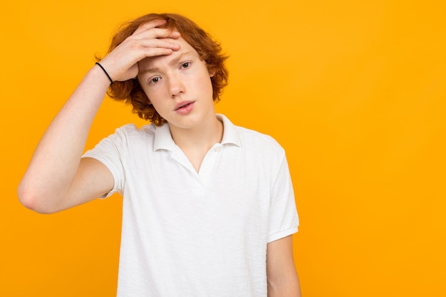 Foto roodharige knappe peinzende blanke tiener man in een wit t-shirt op een gele achtergrond