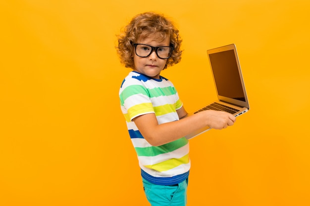 Roodharige krullende jongen verzendt een bericht op laptop op een gele achtergrond