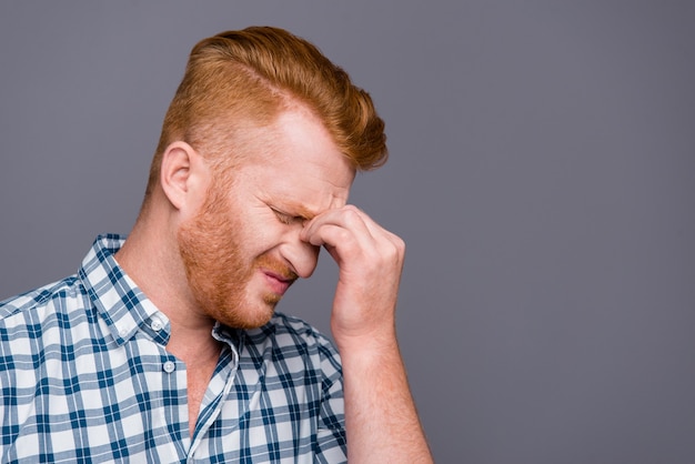 Roodharige man in een blauw geruit overhemd poseren tegen de grijze muur