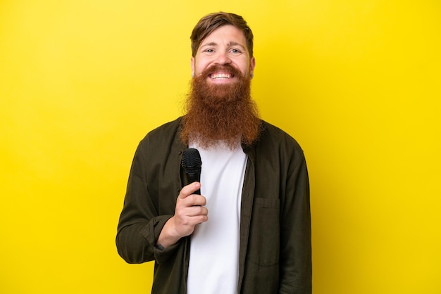 Roodharige man met baard die een microfoon oppakt die op gele achtergrond wordt geïsoleerd en veel glimlacht