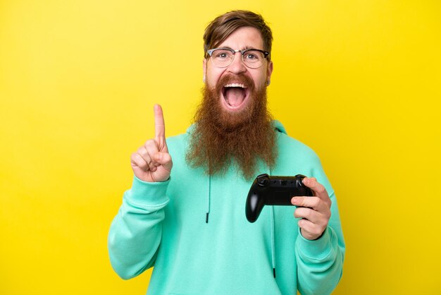 Roodharige man met baard die speelt met een videogamecontroller geïsoleerd op een gele achtergrond die een geweldig idee aangeeft