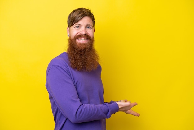 Roodharige man met baard geïsoleerd op een gele achtergrond die zijn handen naar de zijkant uitstrekt om uit te nodigen om te komen