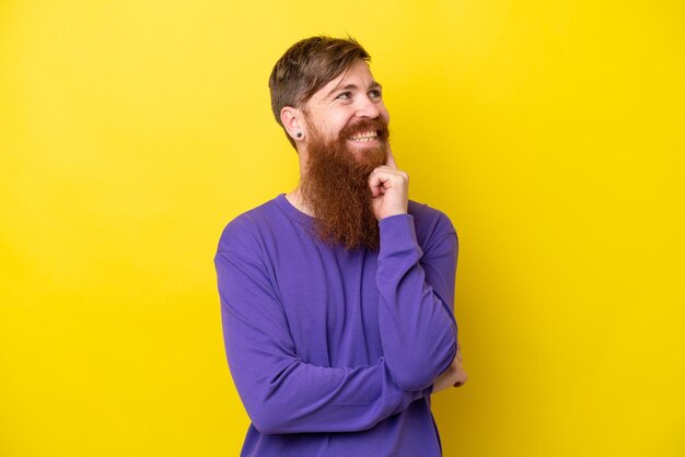 Roodharige man met baard geïsoleerd op gele achtergrond die een idee denkt terwijl hij omhoog kijkt