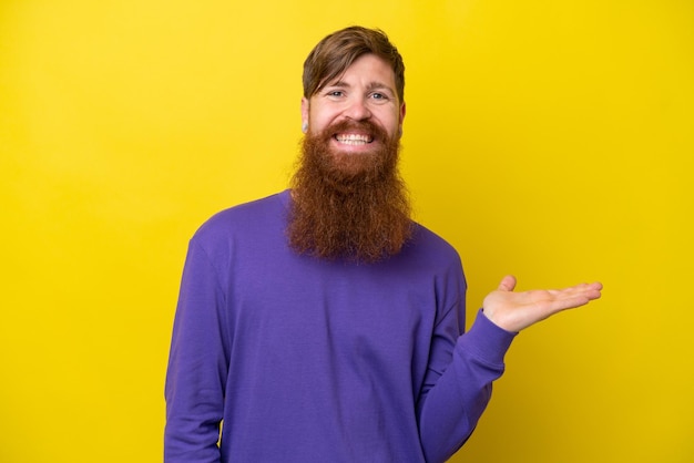 Roodharige man met baard geïsoleerd op gele achtergrond die een idee presenteert terwijl hij glimlacht naar