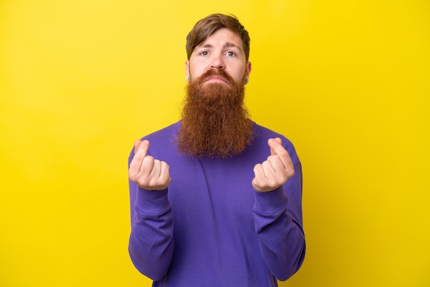 Roodharige man met baard geïsoleerd op gele achtergrond geld gebaar maken maar is geruïneerd