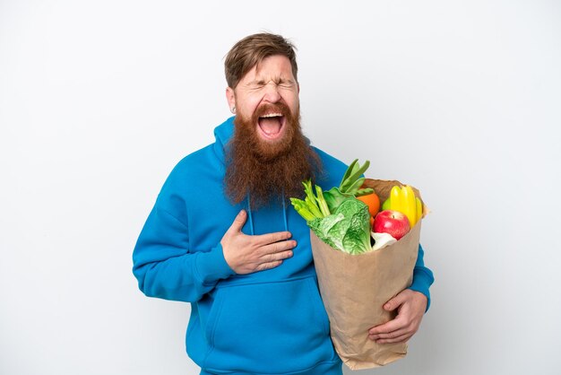 Foto roodharige man met baard met een boodschappentas geïsoleerd op een witte achtergrond glimlachend veel