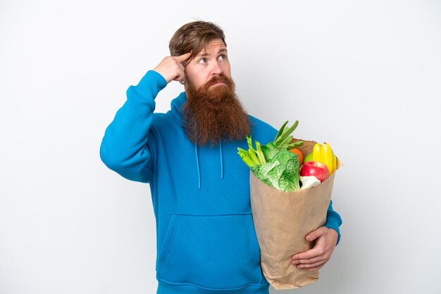 Roodharige man met baard met een boodschappentas geïsoleerd op een witte achtergrond met twijfels en denken