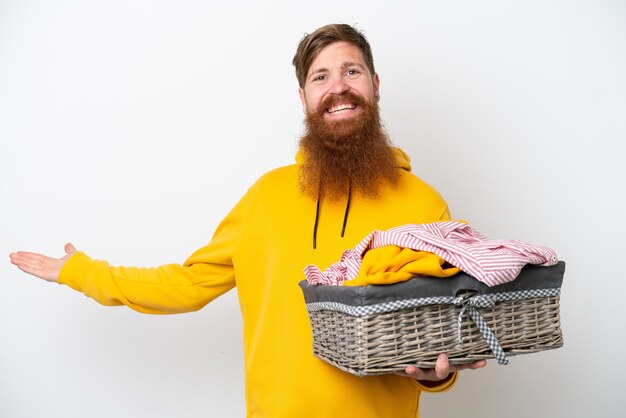 Roodharige man met baard met een wasmand geïsoleerd op een witte achtergrond die zijn handen naar de zijkant uitstrekt om uit te nodigen om te komen