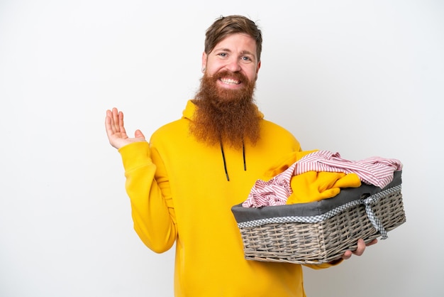 Roodharige man met baard met een wasmand geïsoleerd op een witte achtergrond die zijn handen naar de zijkant uitstrekt om uit te nodigen om te komen