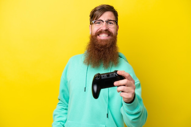 Roodharige man met baard spelen met een video game controller geïsoleerd op gele achtergrond met gelukkige uitdrukking