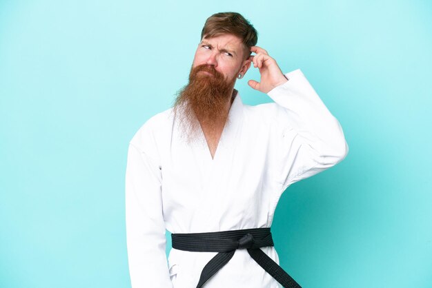 Roodharige man met lange baard die karate doet geïsoleerd op blauwe achtergrond met twijfels