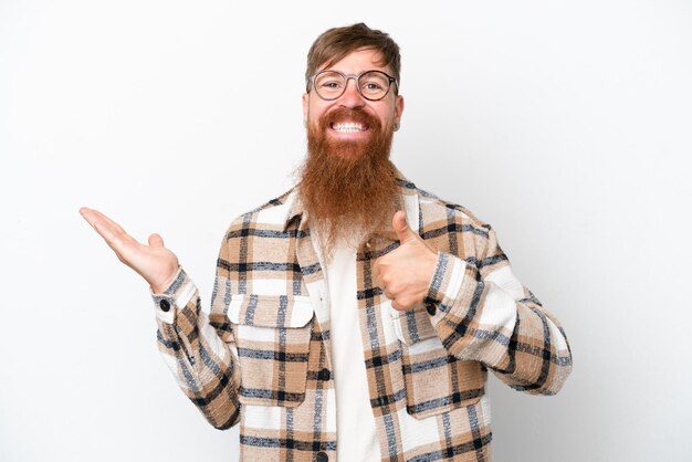 Roodharige man met lange baard geïsoleerd op witte achtergrond met copyspace denkbeeldig op de handpalm om een advertentie in te voegen en met duimen omhoog