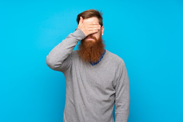 Roodharige man met lange baard over geïsoleerde blauwe bedekkende ogen door handen. Ik wil niets zien