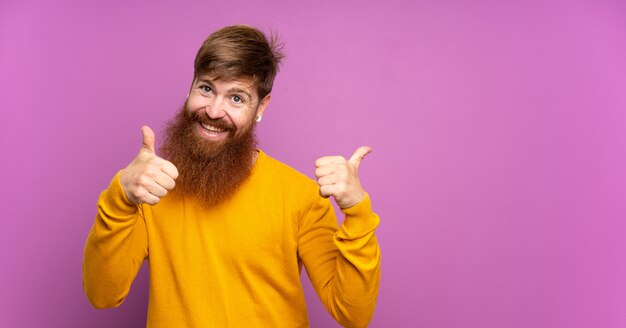 Roodharige man met lange baard over geïsoleerde paars met thumbs up gebaar en lachend