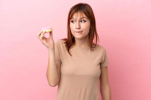 Roodharige meisje geïsoleerd op roze achtergrond met een donut