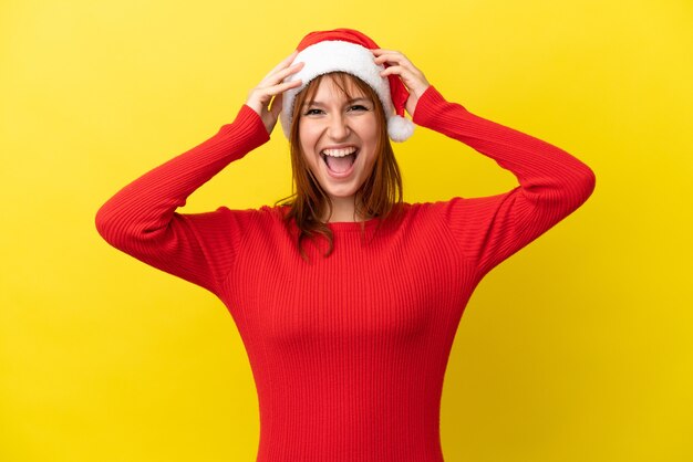 Roodharige meisje met kerstmuts geïsoleerd op gele achtergrond met verrassing expression