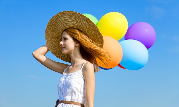 Roodharige meisje met kleur ballonnen op blauwe hemel.