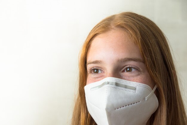 Roodharige meisje met wit masker kijkt recht in de camera met lege ruimte aan de linkerkant van de afbeelding en een witte achtergrond