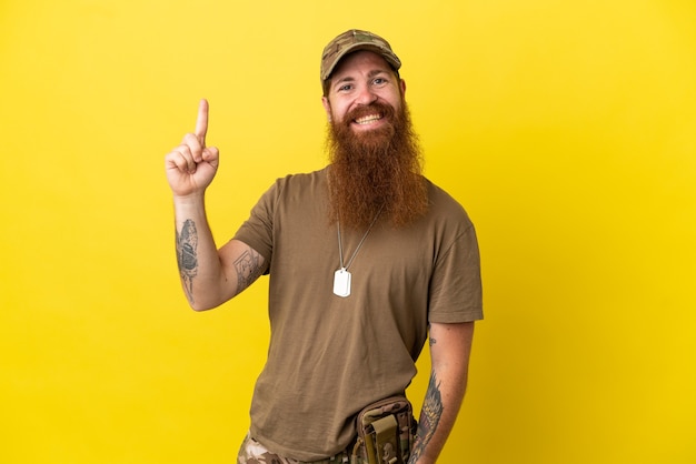 Roodharige militaire man met dog tag geïsoleerd op een gele achtergrond die een vinger toont en opheft in teken van het beste