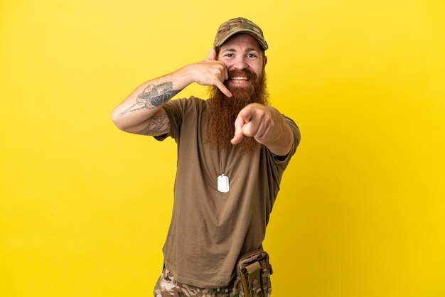 Roodharige Militaire man met dog tag geïsoleerd op gele achtergrond telefoon gebaar maken en naar voren wijzen