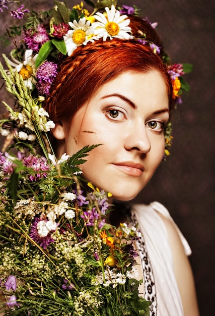 Roodharige model met groot kapsel en bloemen in haar haar en met boeketbloemen.