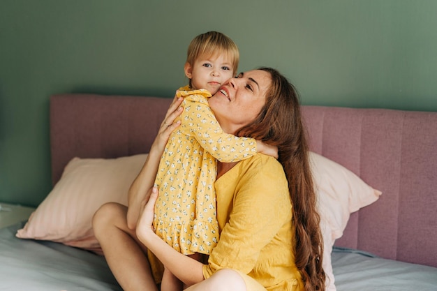 Roodharige moeder knuffelt haar kleine peuter terwijl ze in bed zit