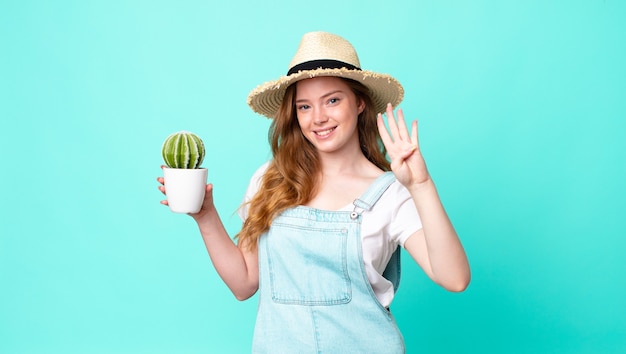 Roodharige, mooie boerenvrouw die lacht en er vriendelijk uitziet, nummer vier toont en een cactus vasthoudt