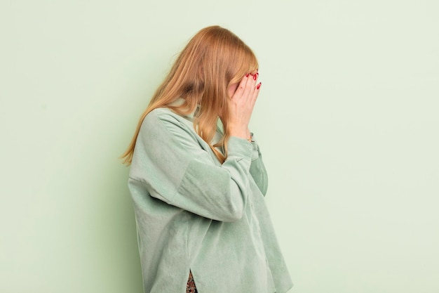 Roodharige mooie vrouw die ogen bedekt met handen met een trieste gefrustreerde blik van wanhoop huilend zijaanzicht