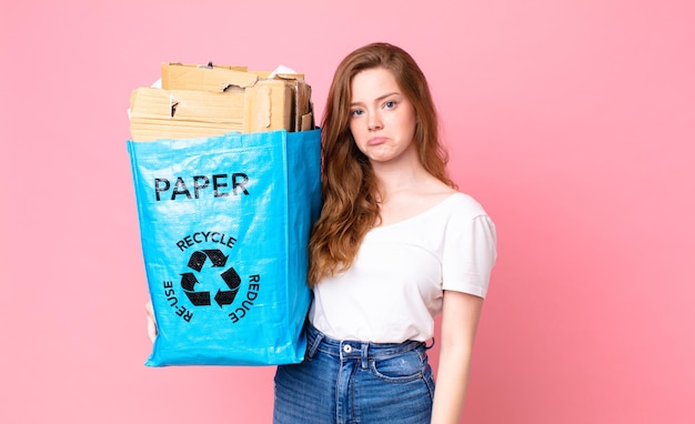 Roodharige mooie vrouw die verdrietig en zeurt met een ongelukkige blik en huilt en een gerecyclede papieren zak vasthoudt