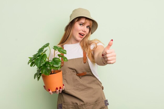 Roodharige mooie vrouw voelt zich trots, positief glimlachend met duimen omhoog. tuinman concept