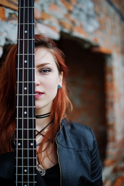 Roodharige punk meisje slijtage op zwart met basgitaar op verlaten plaats portret van gotische vrouw muzikant close-up gezicht van zwartheid persoon met gitaar riff