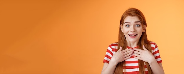 Foto roodharige, schattige meid ontvangt aangenaam nieuws, gecharmeerd, gelukkig, roodharige vrouw drukt handen op borst verbaasde surp